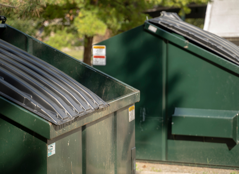 Green dumpsters outside with tree in background